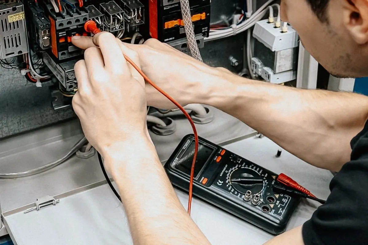 An electrician using test probes and a multimeter at an electrical panel